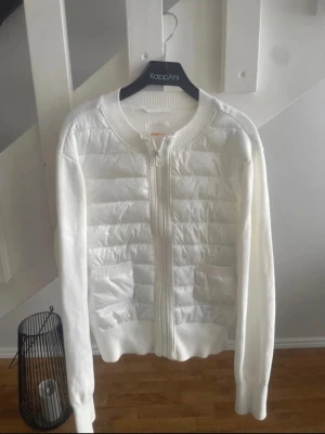 Vit cardiganjacka från Gina Tricot - Snygg vit cardiganjacka från Gina Tricot med quiltade partier framtill och ribbade muddar. Dragkedja hela vägen och två fickor framtill. Perfekt för lager på lager och enkel att matcha med olika outfits.Kan vara nån svart liten fläck på armen men inget som syns enligt mig! 