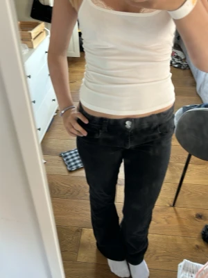 Svarta bootcut mid waist jeans - Säljer ett par svarta jeans bootcut mid waist. Jeansen har klassisk femficksmodell, dubbla knappar i linningen och dragkedja. Materialet är denim med lite stretch för skön passform. Perfekta till en avslappnad och trendig look.