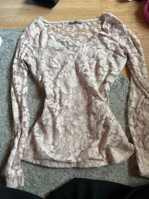 Beige spetsblus från Gina Tricot - Säljer en rosa långärmad spetsblus från Gina Tricot. Blusen har ett genombrutet blommigt spetsmönster och är figurnära i modellen. Säljer då den aldrig används längre