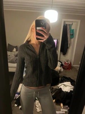 Mörkgrå ribbstickad zip hoodie - Mörkgrå ribbstickad hoodie med dragkedja framtill och långa ärmar. Tröjan har en avslappnad passform och huva, perfekt för en chill look. Materialet ser ut att vara mjukt och bekvämt, idealiskt för att hålla sig varm.