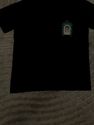 Svart t-shirt Casablanca Avenida - Svart t-shirt från Casablanca med tryck på bröstet som föreställer ett fönster med gröna blad och texten 'Avenida Casablanca'. T-shirten har klassisk passform och är gjord i mjuk bomull. Perfekt för dig som gillar stilrena plagg med coola detaljer.