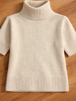 Beige stickad polotröja kort ärm - Säljer en beige stickad polotröja med korta ärmar och bred ribbad kant vid hals, ärmslut och nederkant. Tröjan har en mjuk och stilren look, perfekt för lager på lager. Materialet ser ut att vara ull eller en ullmix.