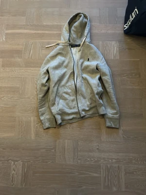 Grå zip hoodie från Polo Ralph Lauren - Säljer en grå hoodie med dragkedja från Polo Ralph Lauren. Klassisk design med huva och vita dragsnören, köpt i usa på Ralph lauren butik