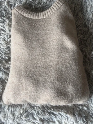 Beige stickad tröja i ullmix - Mysig beige stickad tröja med rund hals och ribbade muddar vid ärmslut och nederkant. Tröjan har en enkel, klassisk design och är tillverkad i mjuk ullblandning som passar perfekt för kyliga dagar.