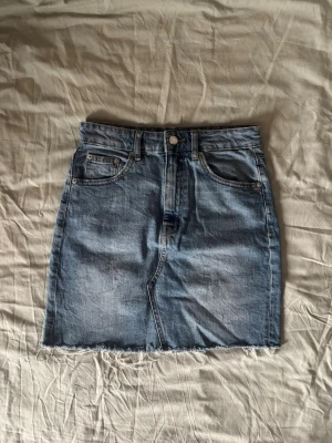 Blå jeanskjol - Säljer en blå jeanskjol i kort modell med slitningar nedtill. 