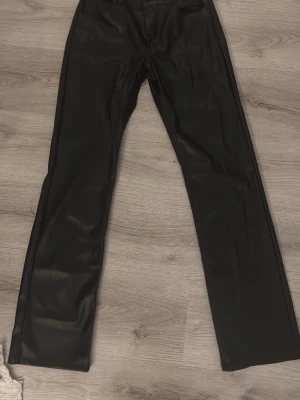 Svarta coated jeans från Bik Bok - Snygga svarta coated jeans från Bik Bok i storlek 38. Byxorna har raka ben, klassisk femficksmodell och en glansig finish som ger en cool läderlook. Perfekta för dig som vill ha en trendig och edgy stil.