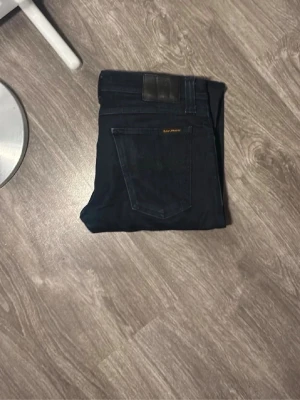 Mörkblå jeans från nudie - Snygga mörkblå jeans från Samsoe Samsoe med klassisk femficksdesign och diskret logga på bakfickan. Jeansen har raka ben och är tillverkade i ett mjukt denim-material som är bekvämt att bära.