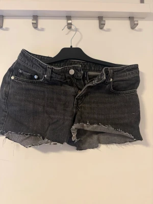 Svarta jeansshorts  - Säljer ett par svarta jeansshorts från weekday  med råa, fransiga kanter. Shortsen har normal passform och knappgylf. 