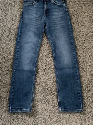 Blå raka jeans från Replay - Säljer ett par klassiska blå jeans från Replay med raka ben och fem fickor. Jeansen har en snygg tvätt med lätt slitning framtill. Tillverkade i slitstarkt denimtyg, perfekta för en avslappnad stil.