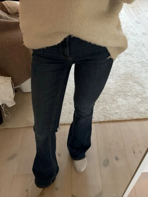 Mörkblå bootcut jeans - Säljer ett par mörkblå bootcut jeans med klassisk femficksdesign och kontrastsömmar. Jeansen har hög midja och är tillverkade i ett stretchigt denimtyg som sitter snyggt. Perfekta till vardagslooken och passar till det mesta.