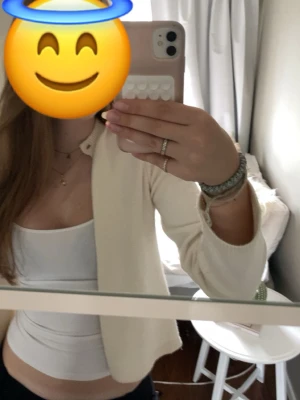 Krämvit kofta med knapp - Trendig krämvit kofta från gina med en knapp upptill. Koftan är ribbstickad längs kanterna och har en rak, croppad passform. Perfekt att bära över ett linne eller t-shirt för en clean och stilren look. Väl omhändertagen och bra skick.