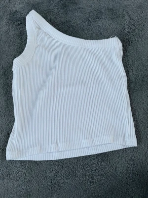 Ribbad oneshoulder topp i vitt och gult - Två ribbade oneshoulder toppar i vitt och gult. Båda är croppade och har en snygg asymmetrisk axelbandslös design. Perfekta för sommarens alla tillfällen och lätta att matcha med jeans eller kjol.
