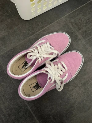 Rosa Vans Old Skool sneakers - Säljer ett par rosa Vans Old Skool sneakers med vit sidostrip och vita snören. Skorna har en klassisk låg profil och är tillverkade i canvas och mocka. Perfekt för dig som vill ha en färgglad och ikonisk look.