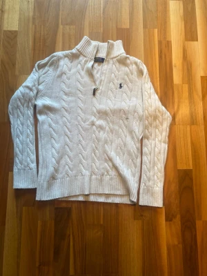Ralph Lauren tröja - Kabelstickad vit tröja från Polo Ralph Lauren med halv dragkedja och ståkrage. Tröjan har ett litet hål i magen men inget större problem. Den är i storlek M men passar både S och M.