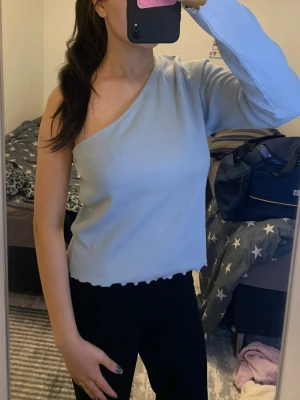 Ljusblå oneshoulder topp - Trendig ljusblå oneshoulder topp med lång ärm och ribbad struktur. Perfekt för dig som vill sticka ut med en unik och stilren look. Toppen är i storlek S passar även som M. 