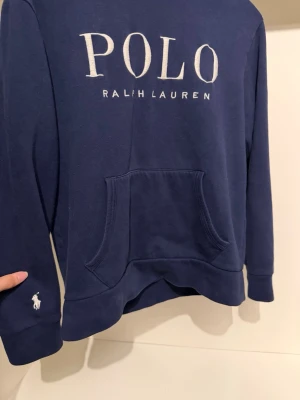 Hoodie Ralph Lauren - Snygg marinblå hoodie från Polo Ralph Lauren med stor logga framtill och klassisk känguruficka. Broderad vit Polo-ikon på ärmen. Tillverkad i mjuk bomullsblandning för skön känsla och stilren look. Passar S perfekt