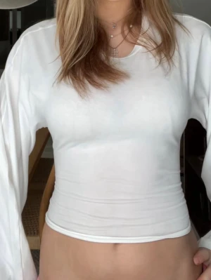 Vit croppad topp med knyt i ryggen - Trendig vit croppad topp med långa ärmar och snygg knytning i ryggen. Toppen har en clean look och är perfekt för dig som gillar stilrena plagg med en twist. Tillverkad i mjukt material som sitter skönt mot kroppen.