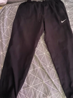 Svart Nike träningsset med hoodie - Säljer ett svart träningsset från Nike med matchande hoodie och byxor. Hoodien har en klassisk huva och Nike-logga på bröstet. Byxorna har resår i midjan och en vit Nike-swoosh på benet. Perfekt för träning eller chill. Materialet är mjukt och bekvämt. Köpt för 1600kr 2025 sommaren 