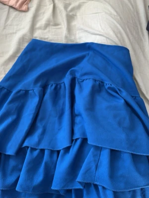 Blå volangkjol med lager - Snygg blå kjol med flera volanglager som ger ett livfullt intryck. Kjolen har en kort längd och är perfekt för dig som vill sticka ut med färg. Tillverkad i ett mjukt tyg som känns bekvämt mot huden.