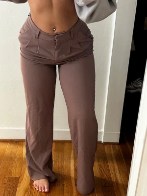 Bruna wide byxor med fickor - Snygga bruna byxor med wide passform och stora fickor framtill. Byxorna har låg midja och är tillverkade i ett mjukt bomullsmaterial. Perfekta för en avslappnad och trendig look.