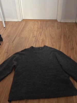 Mörkgrå stickad tröja 157 - Mysig mörkgrå stickad tröja från 157 med rund halsringning och ribbade muddar vid ärmslut och nederkant. Perfekt för kyliga dagar och enkel att matcha med olika outfits.