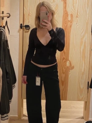 Svart långärmad v-ringad topp - Snygg svart topp med djup v-ringning och långa ärmar. Modellen är croppad och har en figurnära passform som framhäver midjan. 