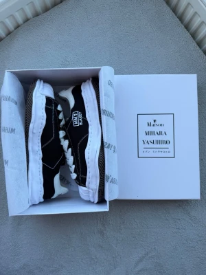 Svarta MMY Blakey sneakers - Unika svarta sneakers från Maison Mihara Yasuhiro med vit sula och kontrastsömmar. Modellen MMY Blakey har chunky, vågig sula och vita snören. Ovandelen är i canvas och detaljerna ger en cool, streetig vibe.