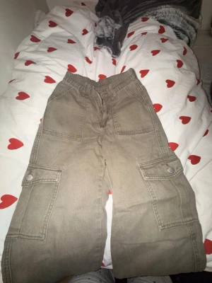 Gröna cargobyxor  - Säljer ett par beiga cargobyxor med bred passform och elastisk midja. Perfekta för en avslappnad och trendig streetstil. Highwaist. Uppsydda för att passa 135-145cm💚