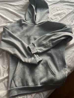 Grå basic hoodie med ficka - En enkel och stilren grå hoodie med huva och stor magficka. Tillverkad i mjukt sweatshirtmaterial och har ribbade muddar vid ärmar och nederkant. Perfekt för en avslappnad och casual look.