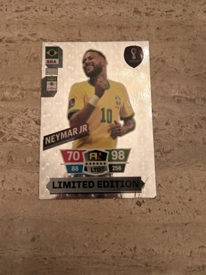 Neymar JR Limited Edition stil:A6 kort - Säljer ett Neymar JR FIFA World Cup Qatar 2022 Limited Edition samlarkort med Neymar Jr från Brasilien. Kortet har glittrig yta, färgerna guld, grön och gul samt detaljerade stats och loggor. Perfekt för samlare av fotbollskort!