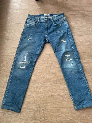 Blå slitna jeans från Replay - Säljer ett par blå jeans från Replay med snygga slitningar och distressed detaljer. Modellen är slim fit. Ny pris 1800 kr. 30/32.