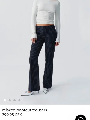 Svarta bootcut kostymbyxor med ränder - Snygga svarta kostymbyxor med vita smala kritstrecksränder och bootcut passform. Byxorna har medelhög midja och vida ben som ger en avslappnad men stilren look. Perfekta för dig som gillar trendiga och bekväma byxor.