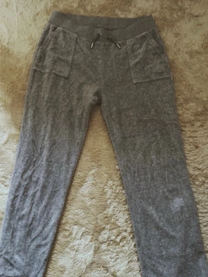 Grå Juicy couture mjukisbyxor med fickor - Jätte snygga grå riktiga Juicy Couture byxor med fina detaljer och fickor i baksidan i storlek L 🤍. Ser jättebra ut på rumpan när man har på sig den. Jätteskönt material och jätte bekvämt i midjan. Perfekt för skolan eller mjukisar hemma och passar jätte bra med ett simpelt topp. Lite utsvängda på bottom och tight i midjan och vid lårna. 🎀