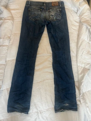 Low waist bootcut jeans - Säljer ett par klassiska blå bootcut jeans med slitningar och snygg tvätt. Jeansen har fem fickor, kontrastsömmar och läderpatch bak i midjan. Tillverkade i bomull med en skön passform och cool vintagekänsla. Storlek W24 i gott skick! Märket är LTC