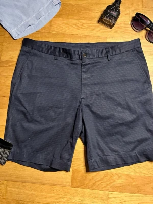 Mörkblå shorts från Sand - Snygga mörkblå shorts från  Sand med diskret mönster och klassisk passform. Shortsen har sidofickor, bakficka med knapp och bälteshällor. Perfekta för sommardagar och stilrena outfits.