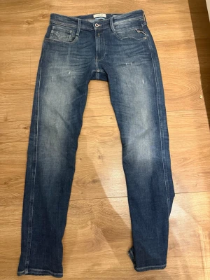 Replay Anbass slim fit jeans blå - Snygga blå slim fit jeans från Replay, modell Anbass. Jeansen har en klassisk femficksdesign, lätt slitna detaljer och en tvättad look. Perfekta för dig som gillar en modern och avslappnad stil. Materialet är bomull med stretch för extra komfort.