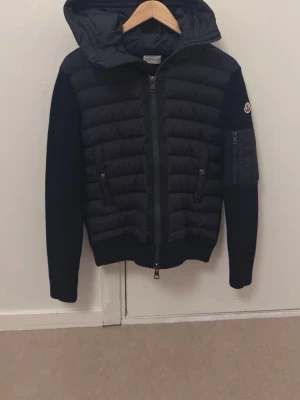 Moncler mörkblå cardigan - Moncler cardigan i mörkblå färg. Väldigt stilren modell med quiltad framsida och huva samt stickade ärmar för en sportig och bekväm passform. Klassisk Moncler-patch på armen och dragkedjeficka på ärmen.  Perfekt som vår/höst-jacka eller lager på lager under kallare dagar.  • Färg: Mörkblå • Dragkedja framtill • Två framfickor + ficka på ärmen • Nytt skick  Säljes då den inte passar. Skicka gärna meddelande vid frågor 😊