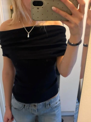 Svart offshoulder topp - Snygg svart offshoulder topp med tight passform. Toppen är ärmlös och har en bred kant upptill som ger en stilren look. Perfekt att matcha med jeans eller kjol för en trendig outfit. Passar XS-M