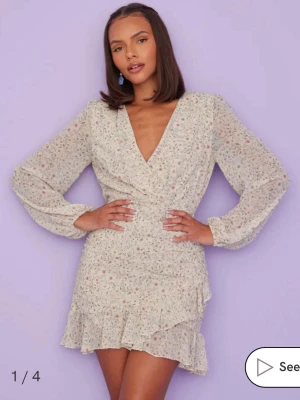 klänning  - Supersöt kort omlottklänning med blommigt mönster i pastellfärger. Klänningen har långa ärmar, v-ringning och volangdetalj nertill. 