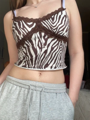 Zebramönstrad brun och vit linnetopp - Trendigt zebramönstrad linnetopp i brunt och vitt med spetsdetaljer längs bysten. Topp med smala axelband och croppad passform, perfekt för en cool och avslappnad stil. Materialet känns mjukt och följsamt mot huden.