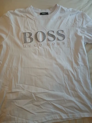 Hugo Boss t shirt vit - Vit t-shirt från Hugo Boss med stort BOSS-tryck och texten HUGO BOSS på bröstet. Klassisk passform och rund halsringning. Tillverkad i bomull.
