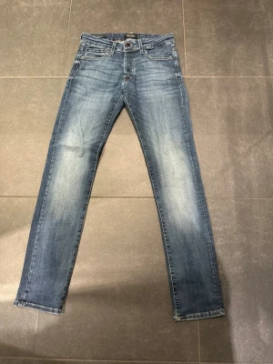 Blå slim fit jeans  - Tja säljer ett par Snygga blå jeans från Jack and Jones Tillverkade i denim med en tvättad look som ger en avslappnad vibe. Perfekta för dig som gillar en enkel men stilren stil.