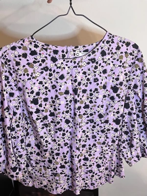 Lila blommig M (44) - Blus i lila med blommigt mönster i svart, vitt och olivgrönt från C Studio. Rund halsringning och puffiga långärmar. Det står storlek 44 men för mig som har L så passar den inte så skulle jag säga att det är storlek M