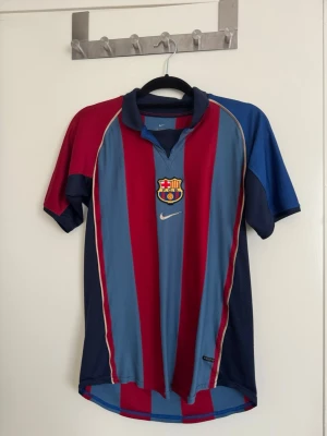 Barcelona fotbollströja Nike - Klassisk Barcelona fotbollströja från Nike med klubbmärke på bröstet. Tröjan har blå och röda vertikala ränder, korta ärmar och krage. Perfekt för dig som älskar fotboll och vill representera ditt favoritlag. Size XL kids eller S men / bra skick lite Sten på bak sidan annars bra  