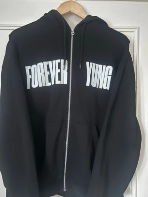 Forever yung lean hoodie - Säljer en svart hoodie med dragkedja och stora vita tryck fram och bak. På framsidan står det 'FOREVER YUNG' och på ryggen 'LEAN'. Hoodien har huva med snören och känguruficka. Köpt på pop upen i Stockholm  