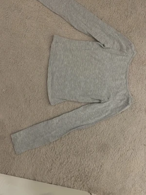 Ljusgrå långärmad topp - En enkel och stilren ljusgrå långärmad topp med rund halsringning. Tillverkad i ett mjukt och stretchigt material som sitter skönt på kroppen. Perfekt att matcha med jeans eller kjol för en clean look.