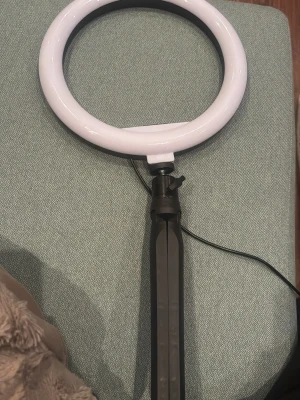Rund ringlampa med stativ - Säljer en rund ringlampa i vit plast med svart stativ och USB-kabel. Perfekt för streaming, smink eller foto. Lampan ger ett jämnt och starkt ljus och är enkel att justera tack vare det flexibla stativet.