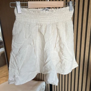 Linneshorts från BERSHKA  - Luftiga beiga shorts med bred resår i midjan och avslappnad passform. Tillverkade i ett mjukt bomullsliknande material, perfekta för varma dagar. Stilsäkra och enkla att matcha med olika toppar.
