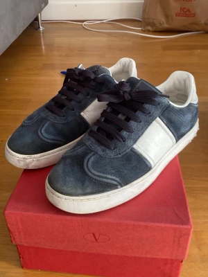 Valentino flycrew - Snygga sneakers i blå mocka med vita detaljer och svart snörning. Skorna har en klassisk låg siluett och vit sula med unik mönstring undertill. Perfekta för dig som vill ha en stilren och trendig look.