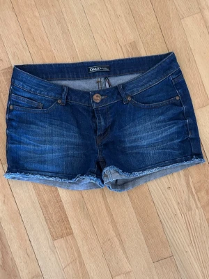Mörkblå low waist jeansshorts från ONLY - Snygga mörkblå jeansshorts från ONLY med fransig kant nertill. Låg midja stl 29”. Perfekta för varma dagar och enkel att matcha med olika toppar.